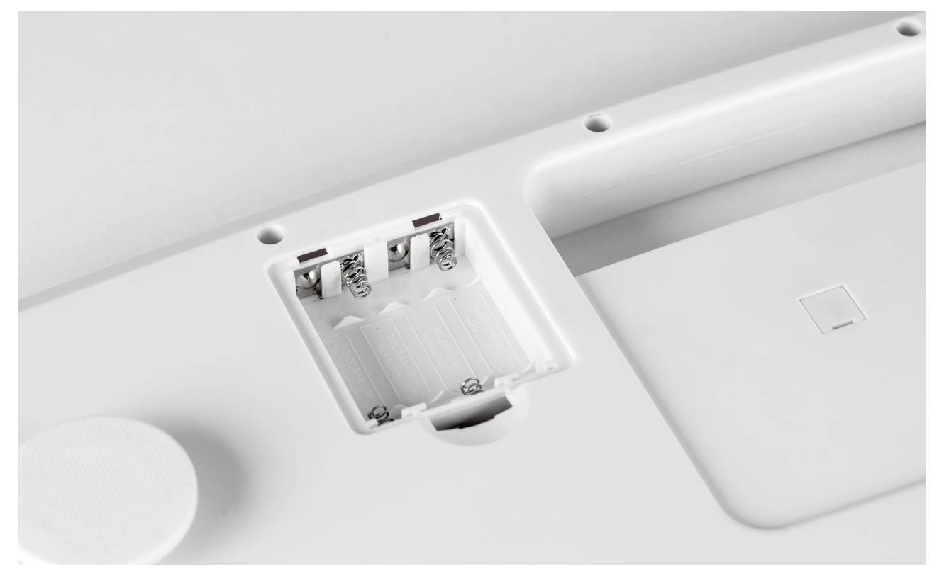 Een geopende batterijklep van een elektronisch apparaat met lege batterijhouders en zichtbare veren.