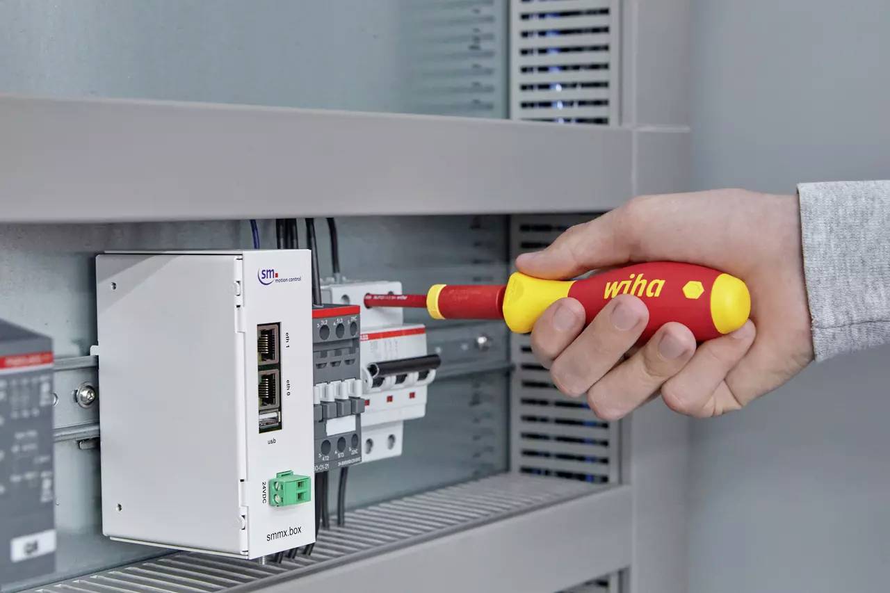 Een persoon draait een schroef op een stroomonderbreker paneel aan met behulp van een geel en rood schroevendraaier in een bedieningskast.