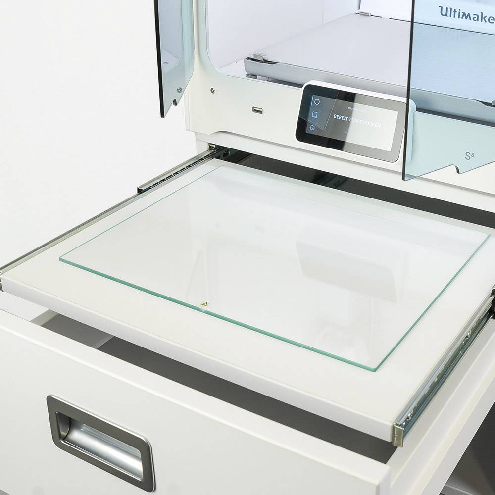 3D-printer met glazen bed in lichte omgeving. Monitor op de voorkant toont display-informatie.