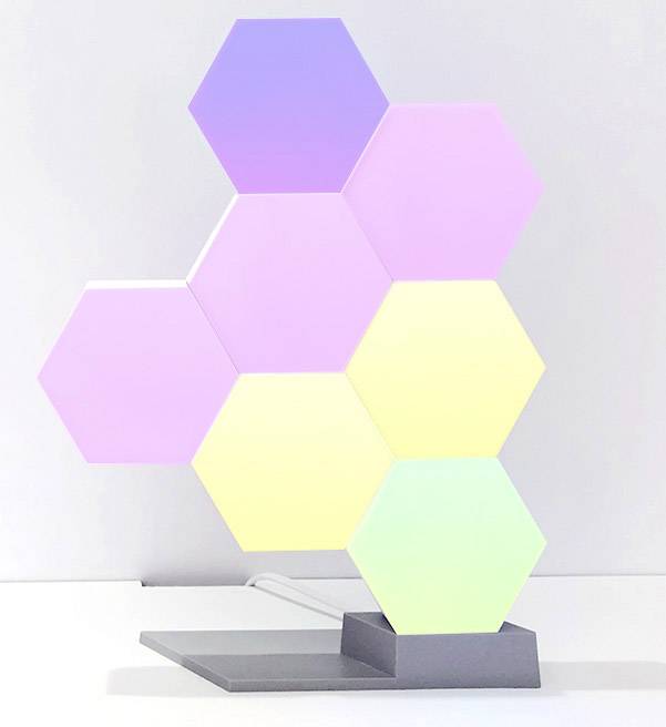 Zeshoekige LED-verlichting in pastelkleuren op een grijze standaard, decoratief geplaatst, creëert een zachte sfeer.