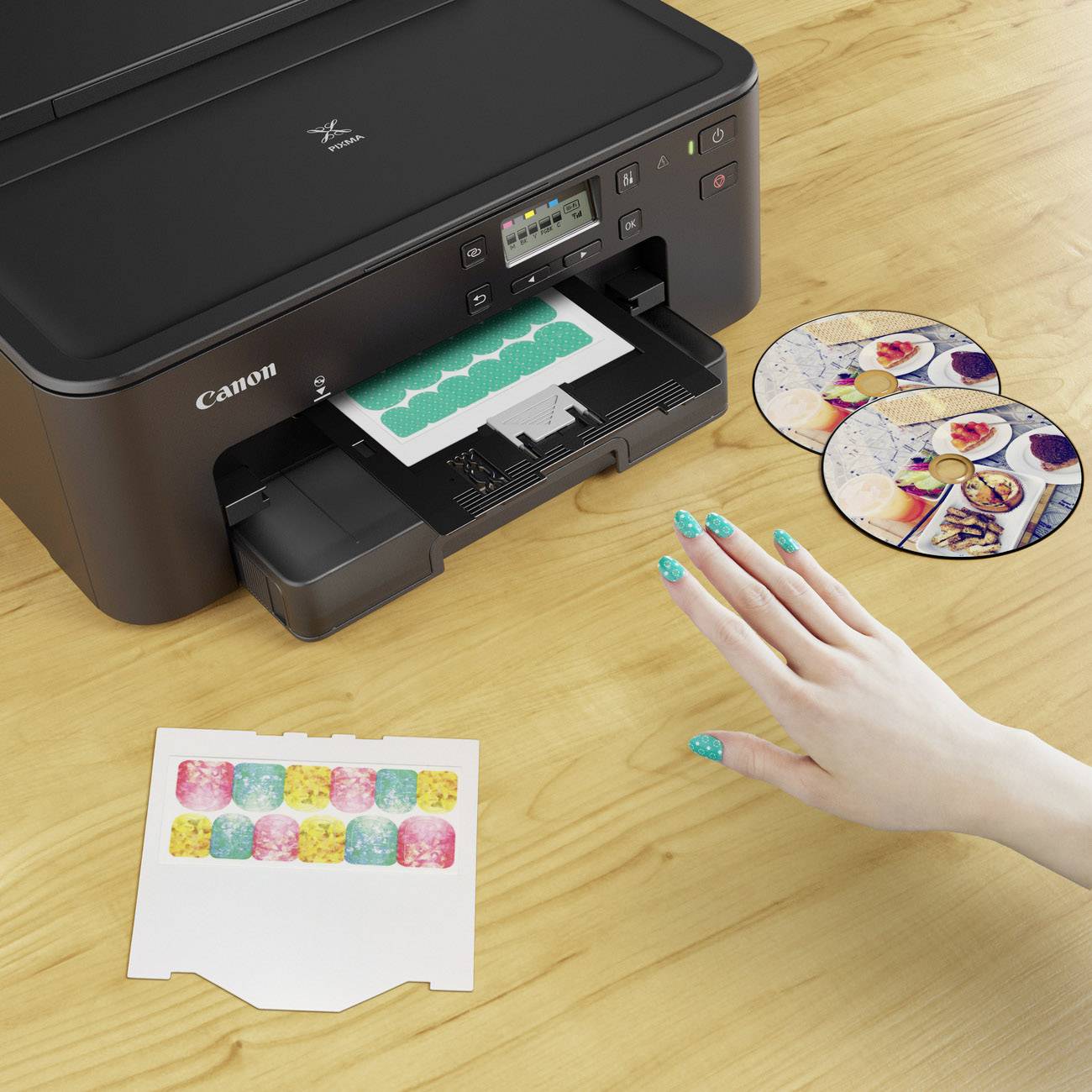 Een printer op een houten tafel. Een hand met turquoise nagelswijst naar een bedrukt papier met kleurrijke patronen. Naast de printer liggen bedrukte cd's.