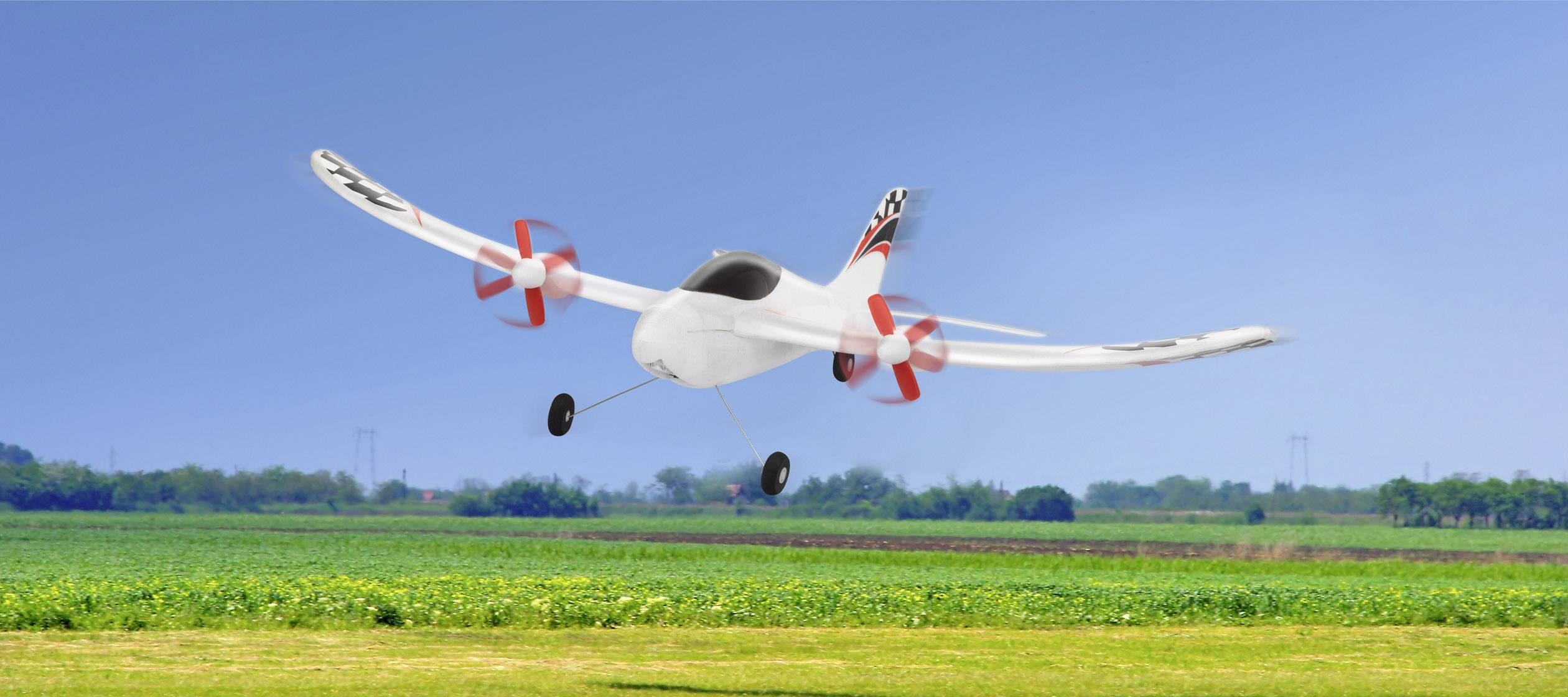 Een klein modelluchtvaarttuig vliegt boven een groen veld, met een blauwe lucht op de achtergrond.