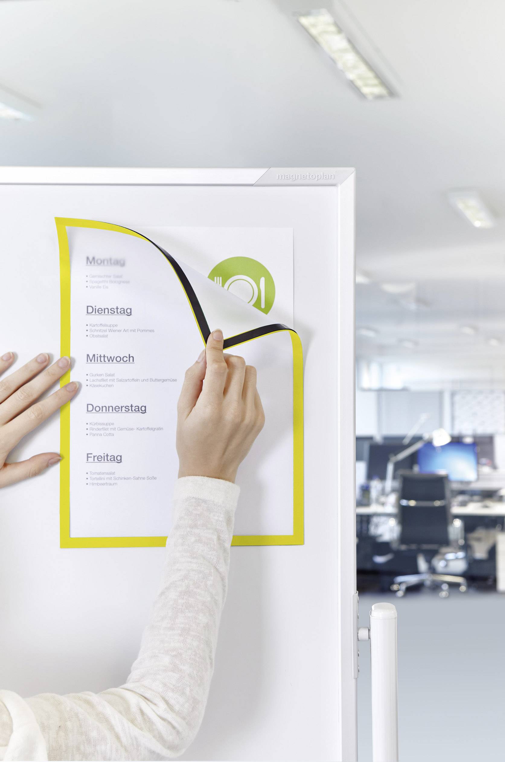 Een persoon hangt een weekplanning met de werkdagen van maandag tot vrijdag op aan een whiteboard in het kantoor.