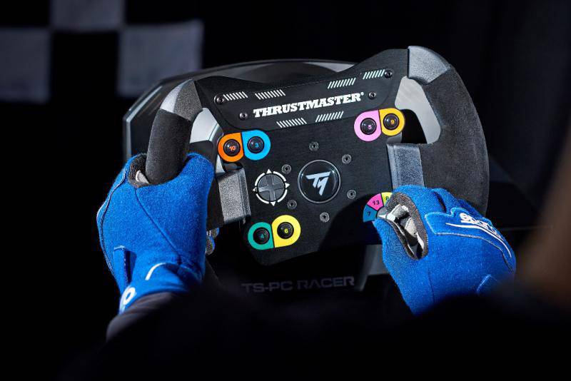 Een persoon draagt blauwe handschoenen en houdt een Thrustmaster racestuur vast voor een donkere achtergrond.