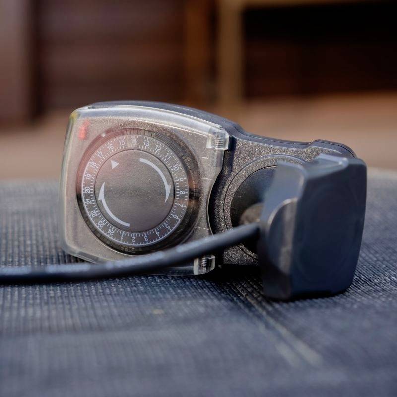 Een close-up van een mechanische timer met een instelbare wijzerplaat waarop tijdsintervallen worden weergegeven. De timer is geplaatst op een gestructureerd oppervlak.