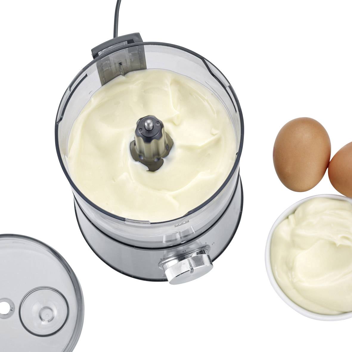Een mixer met witte crème, naast twee eieren en een kom met vergelijkbare crème op een wit oppervlak.