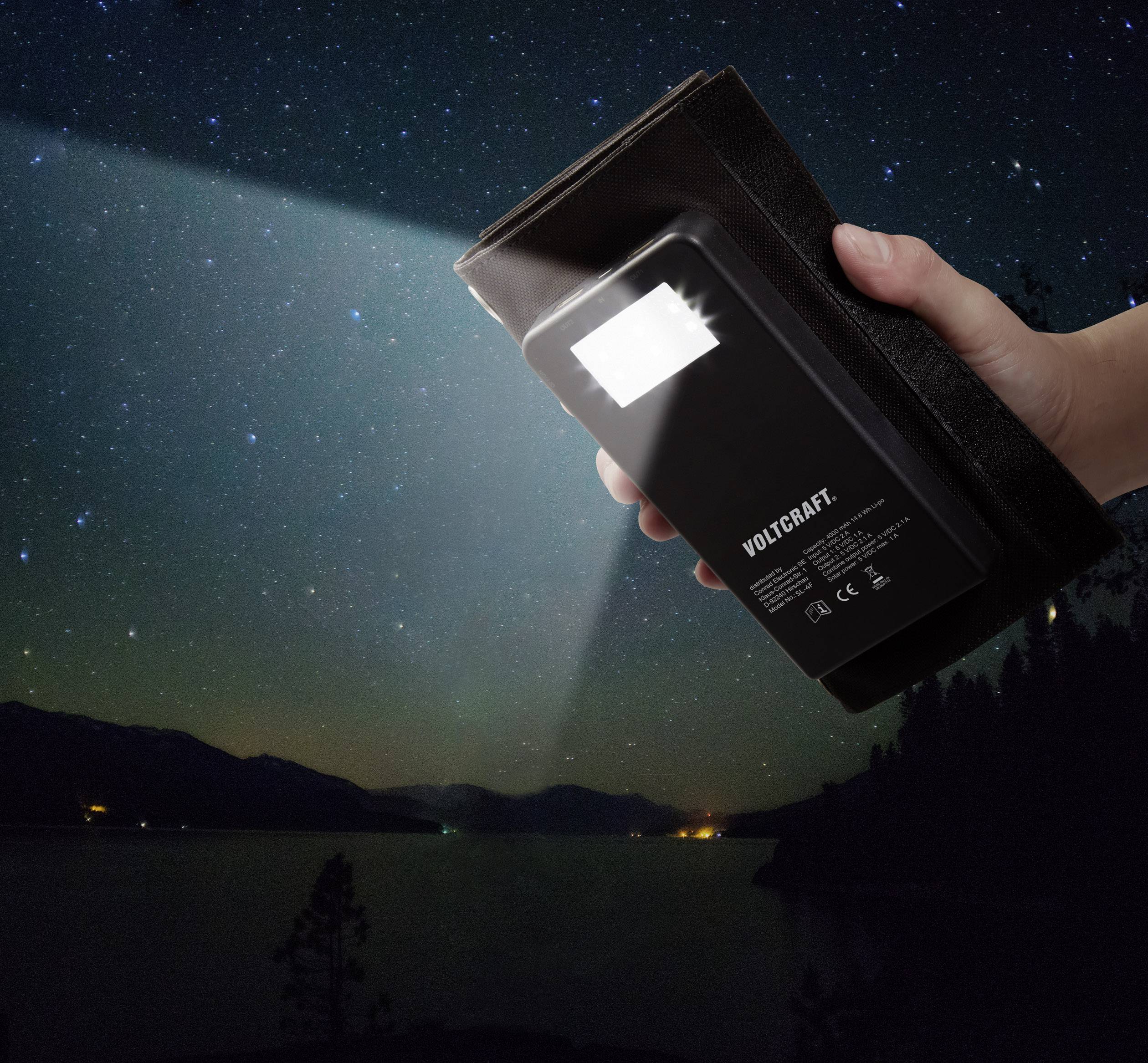 Een hand houdt een zwarte powerbank vast die in de nachtelijke hemel boven een meer schijnt. De hemel is stikhelder met sterren.