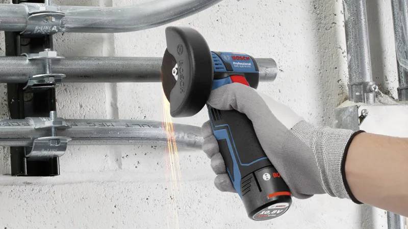 Een persoon die een Bosch haakse slijper gebruikt om metalen buizen door te snijden, waarbij vonken rondvliegen. De persoon draagt een grijze handschoen als veiligheidsmaatregel.