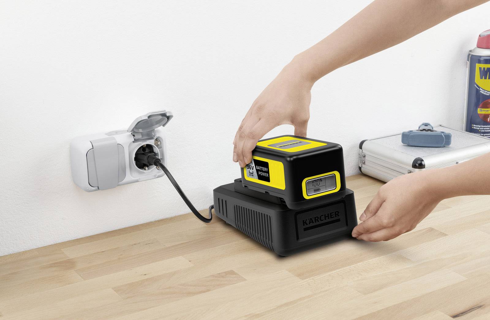 Een persoon plaatst een gele accu op een oplader op een houten tafel, aangesloten op een stopcontact.