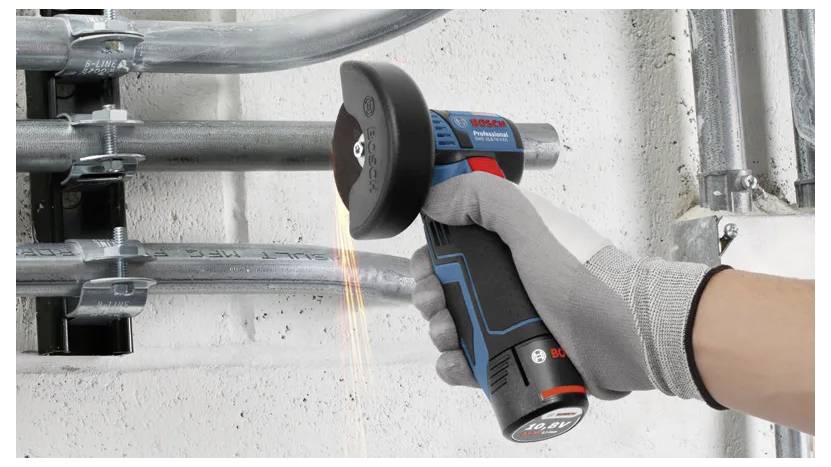 Handschoengeklede hand die een draadloos elektrisch gereedschap met een snijschijf op een metalen buis gebruikt, wat vonken produceert in een industrieel werkgebied.