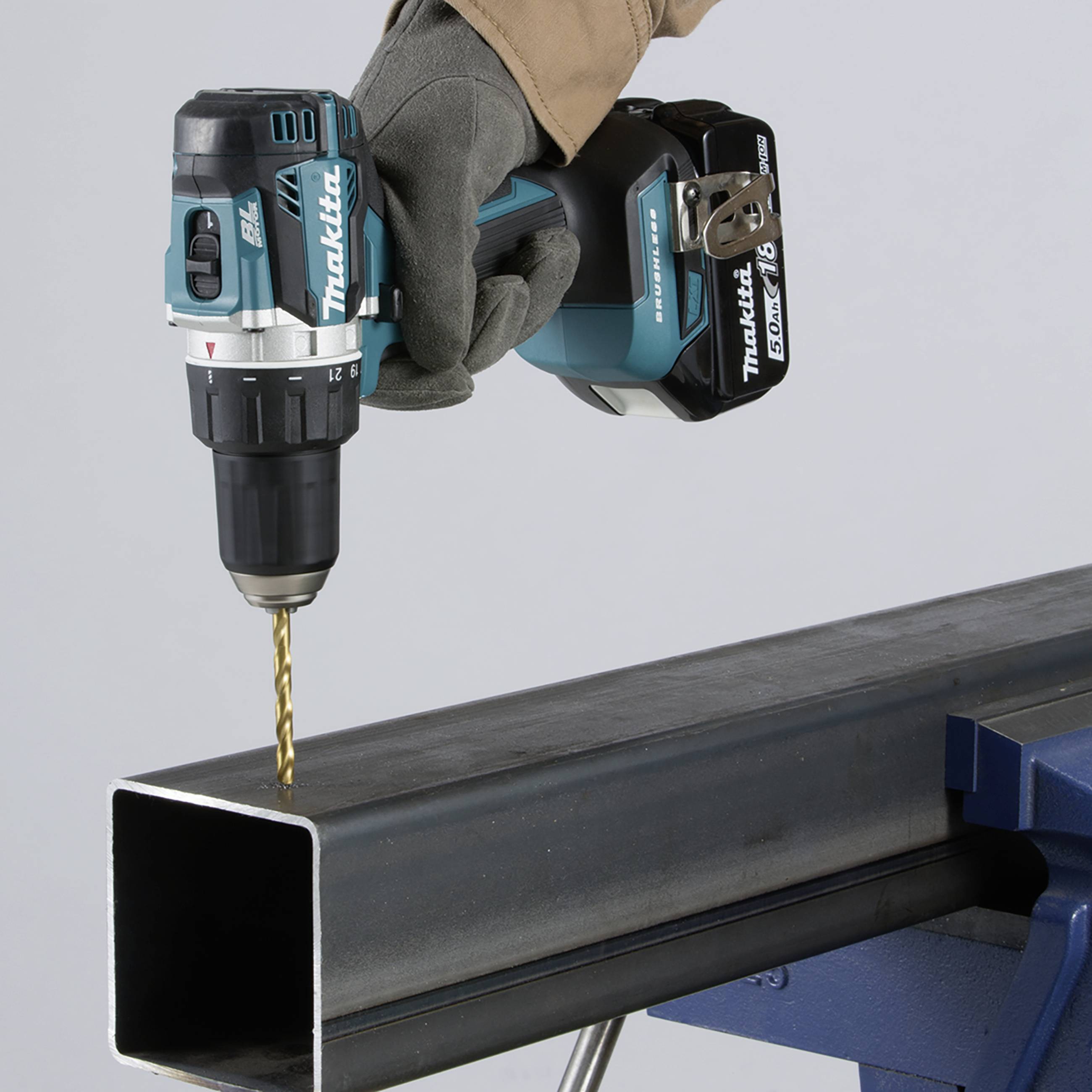 Een persoon houdt een accuboormachine en boort een gat in een stalen ligger. Het gereedschap is blauw en zwart.