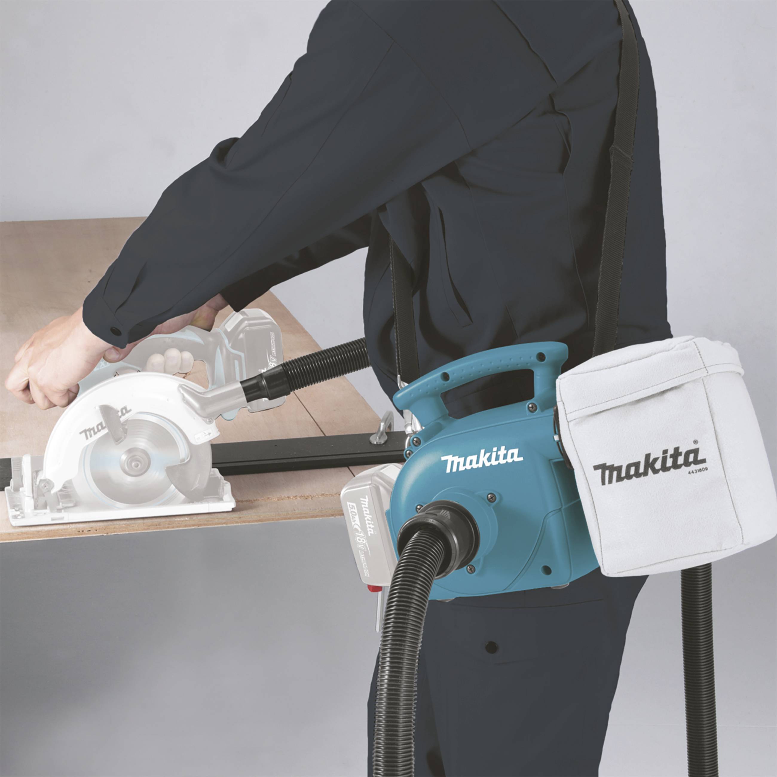 Een persoon zaagt hout met een elektrische Makita handcirkelzaag. Zaagstof wordt verzameld in een aangesloten opvangzak.