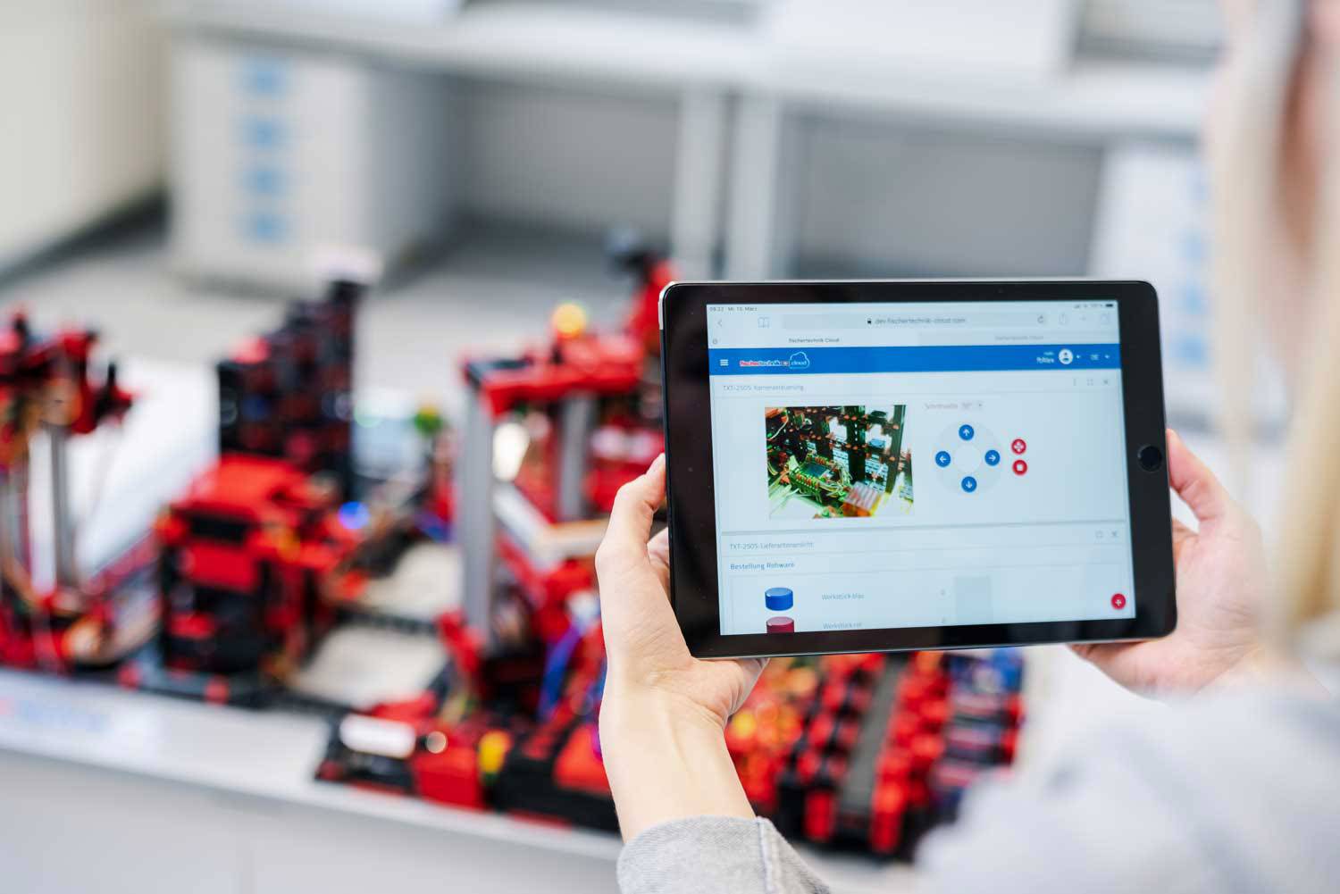 Een persoon houdt een tablet met een technische tekening. Op de achtergrond bevindt zich een model van rode bouwstenen.