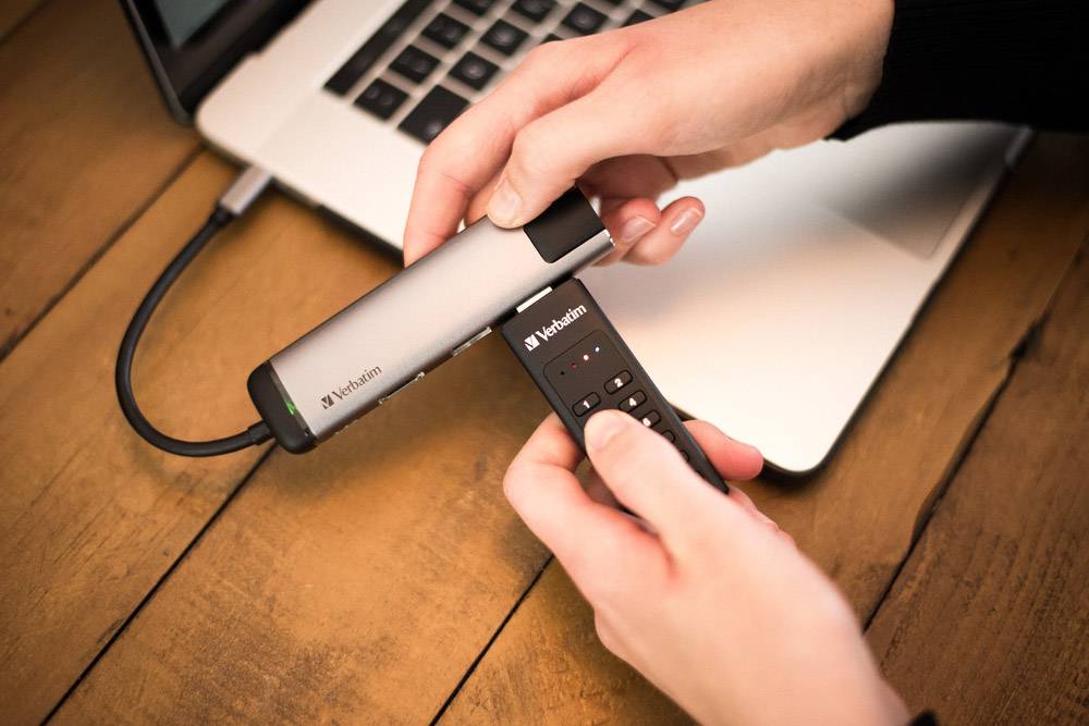 Persoon houdt een Verbatim USB-stick en een draadloze presentatie-afstandsbediening vast boven een laptop, klaar voor gebruik.