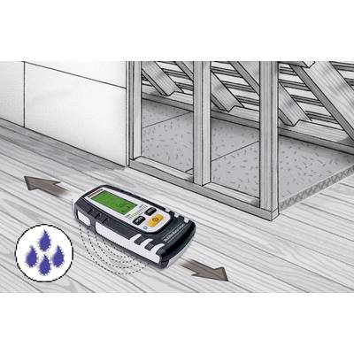 Een vochtmeter wordt over een houten vloer bewogen om de vochtigheid te controleren. Op de achtergrond is een open wandstructuur zichtbaar.