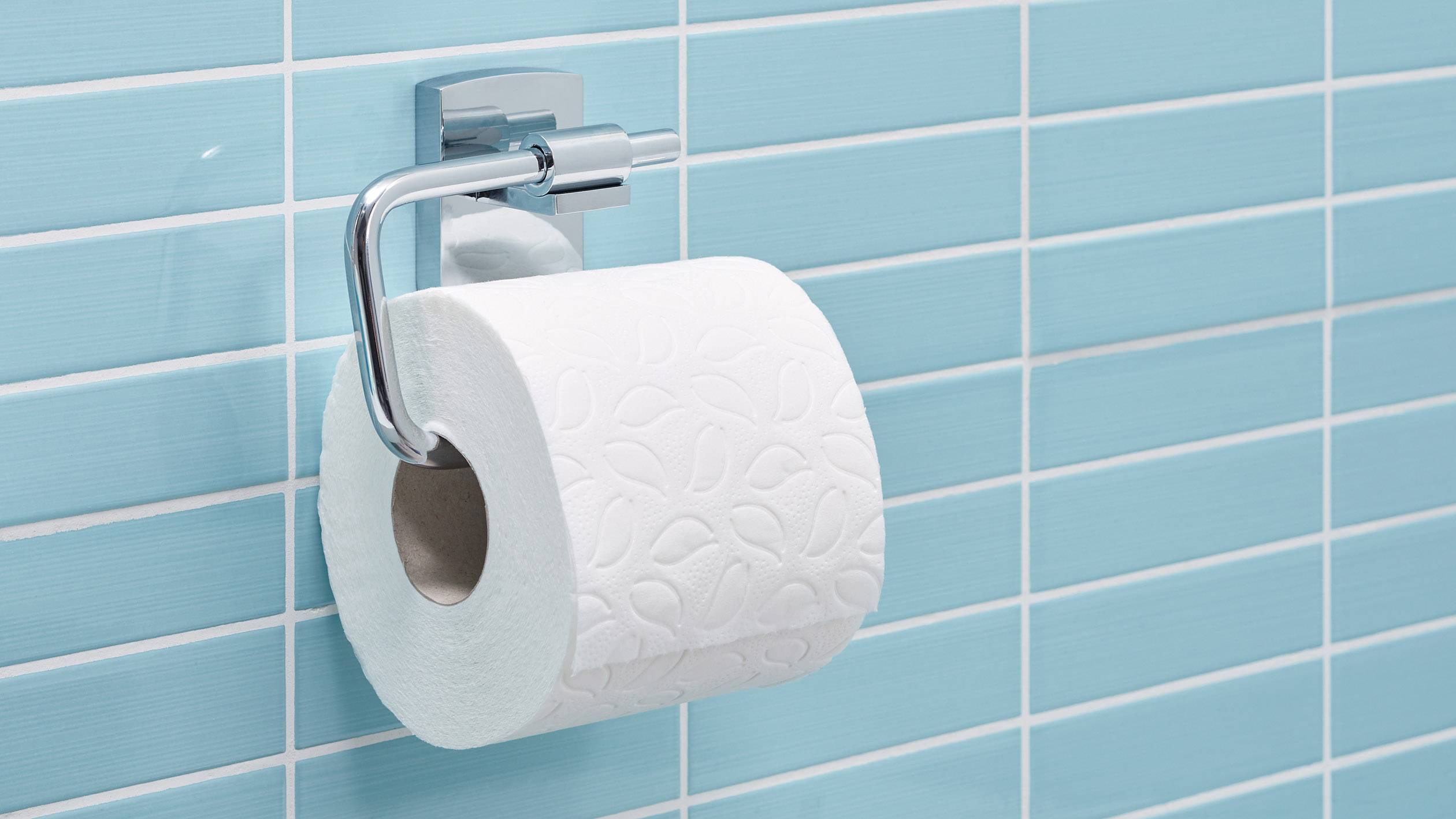 Rol toiletpapier hangt aan een muurhouder voor een blauw betegelde wand.
