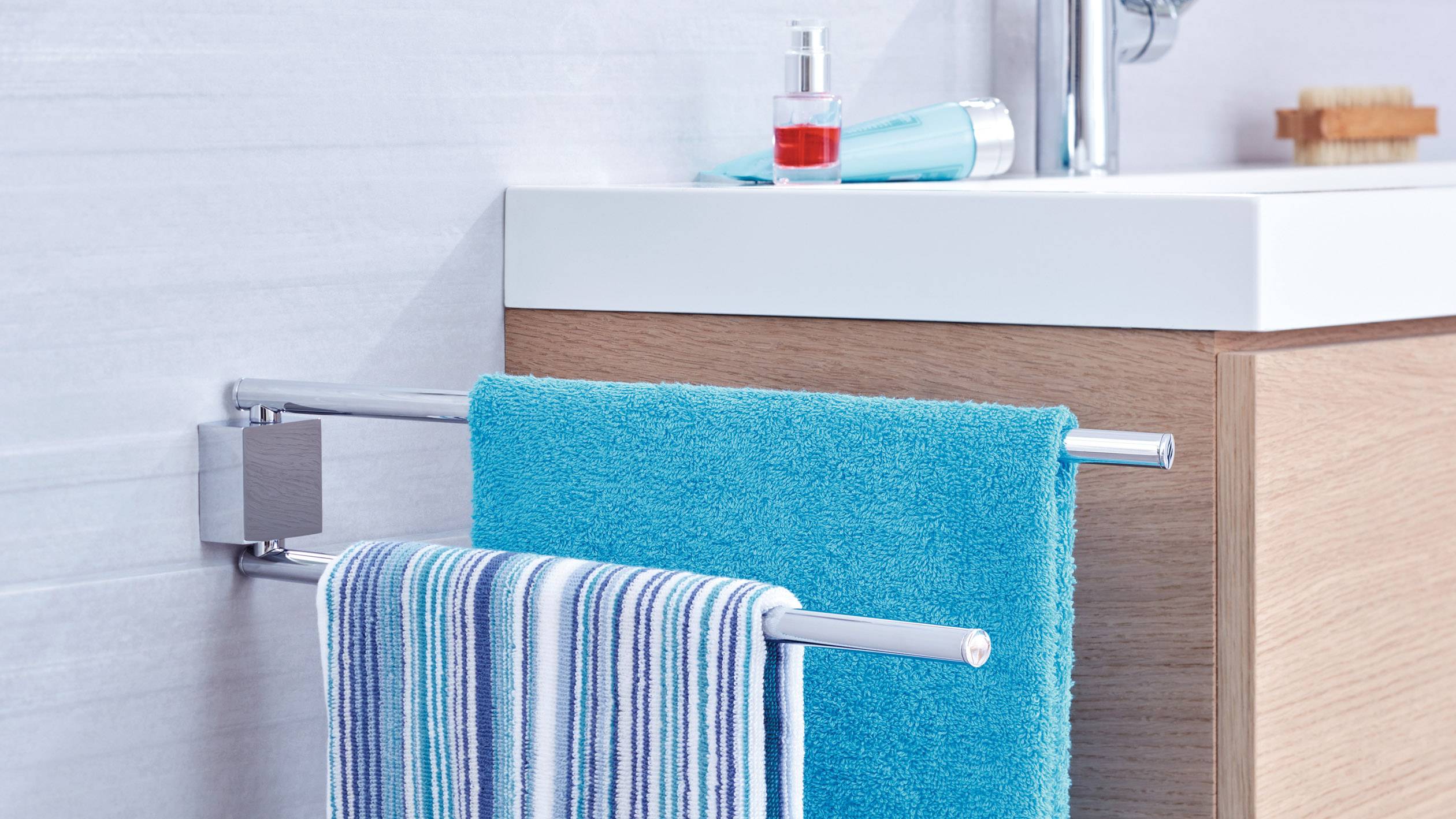 Een badkamer met een handdoekhouder waarop een gestreepte en een turquoise handdoek liggen. Op de achtergrond een wastafel met zeeppomp.