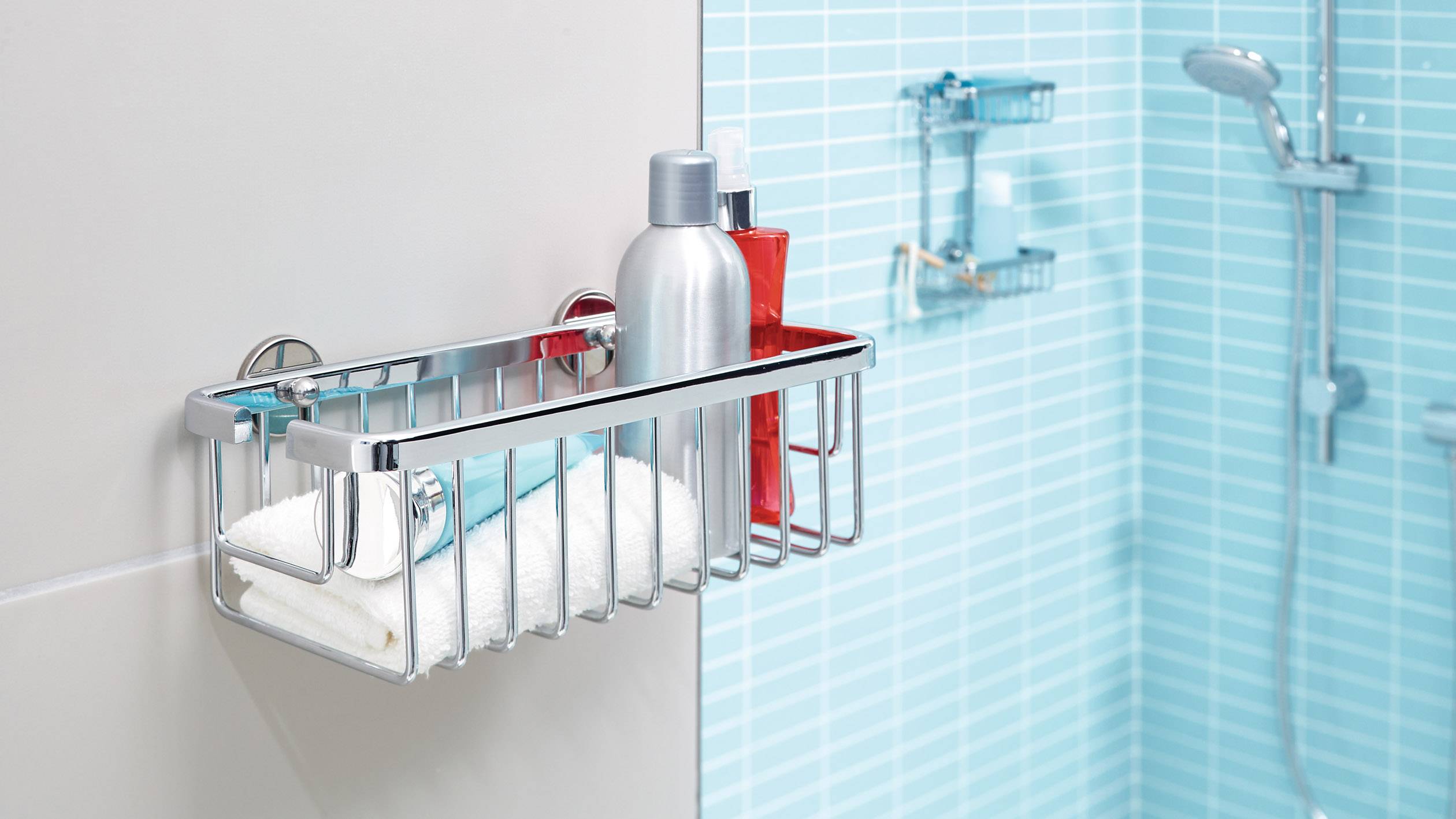 Een metalen doucherek aan een betegelde muur, met shampooflessen en een handdoek in een modern badkamer.