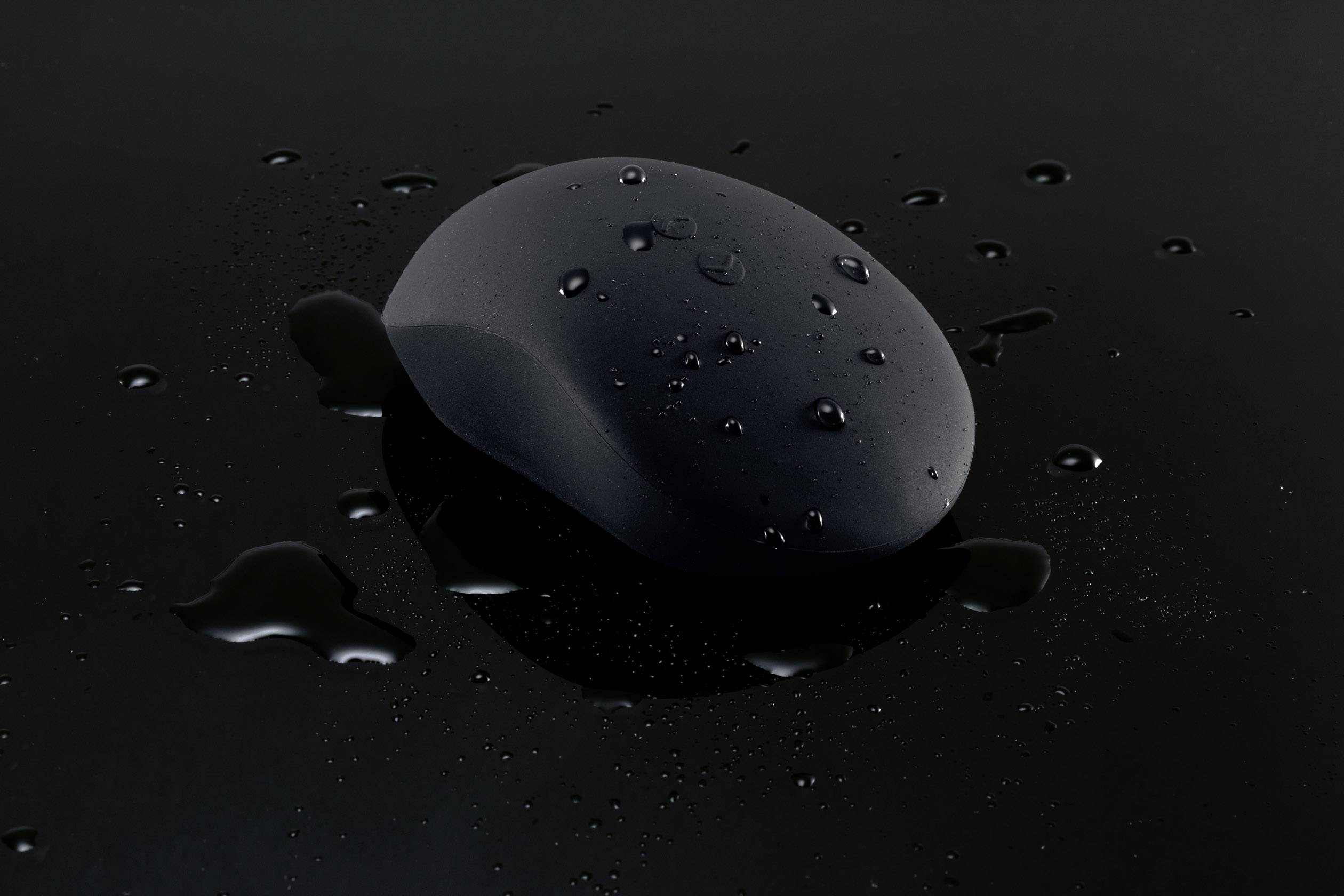 Zwarte computermuis met waterdruppels op zwarte achtergrond, mogelijk een waterbestendig model illustrerend.