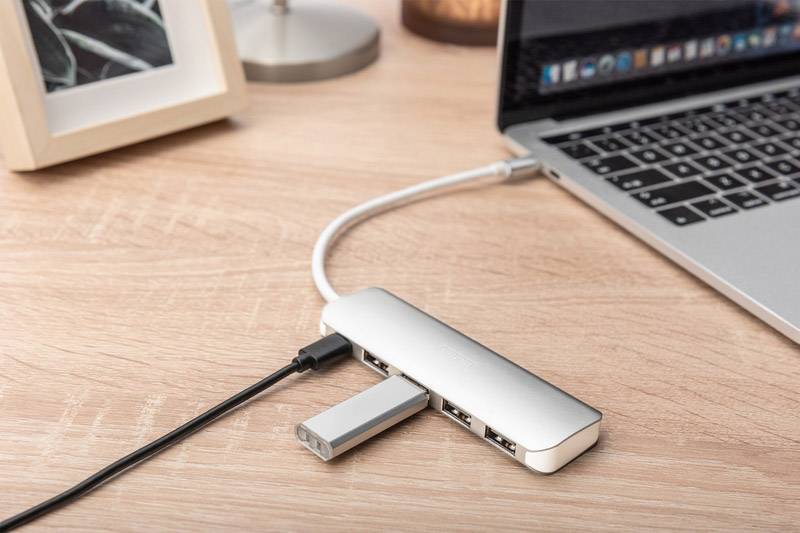 USB-hub met meerdere aansluitingen, waaronder USB-sticks, aangesloten op een laptop. De adapter ligt op een houten tafel.