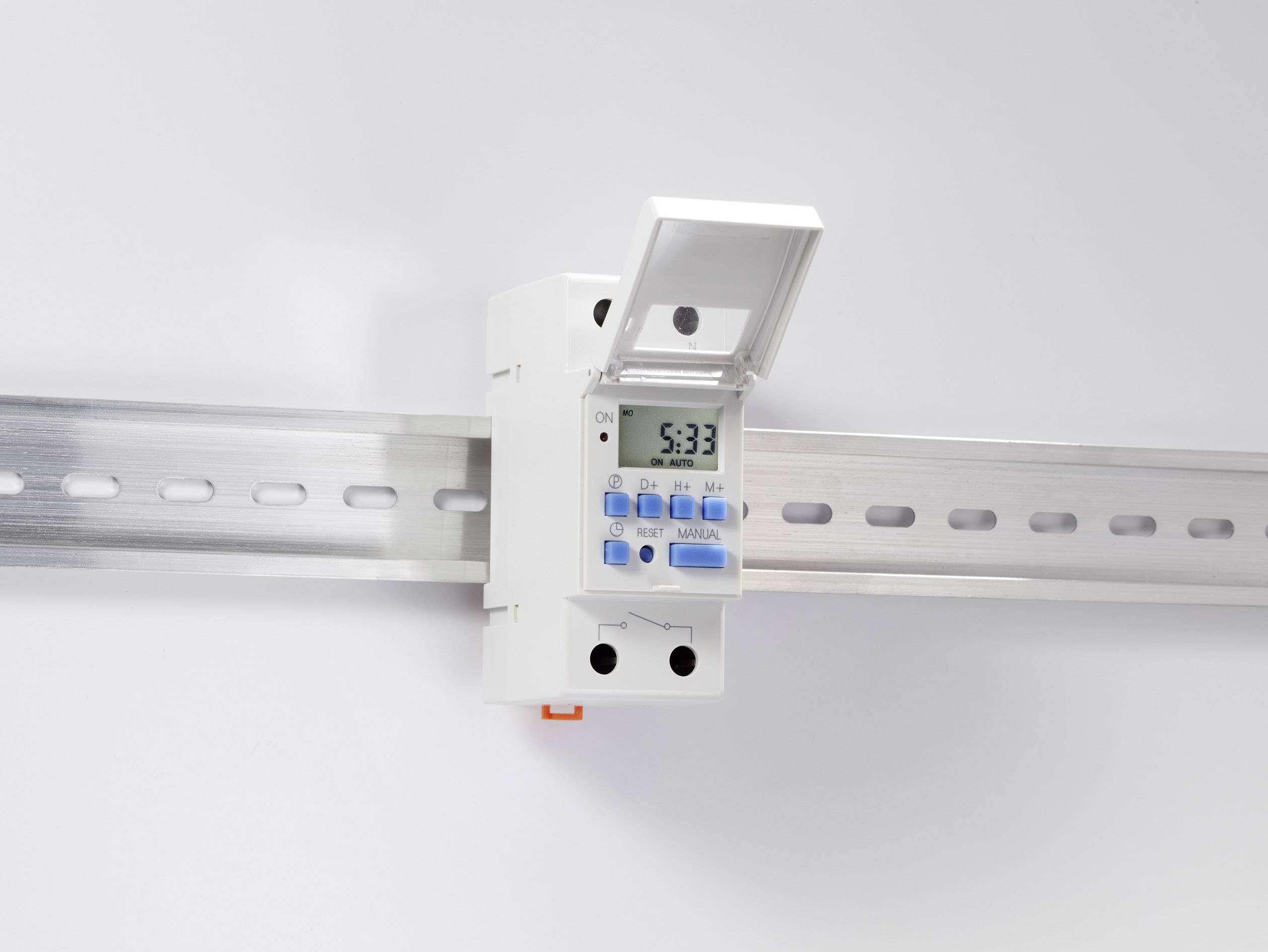 Een digitale tijdschakelaar is gemonteerd op een DIN-rail. Het display toont '5:33'. Een klep is licht geopend.