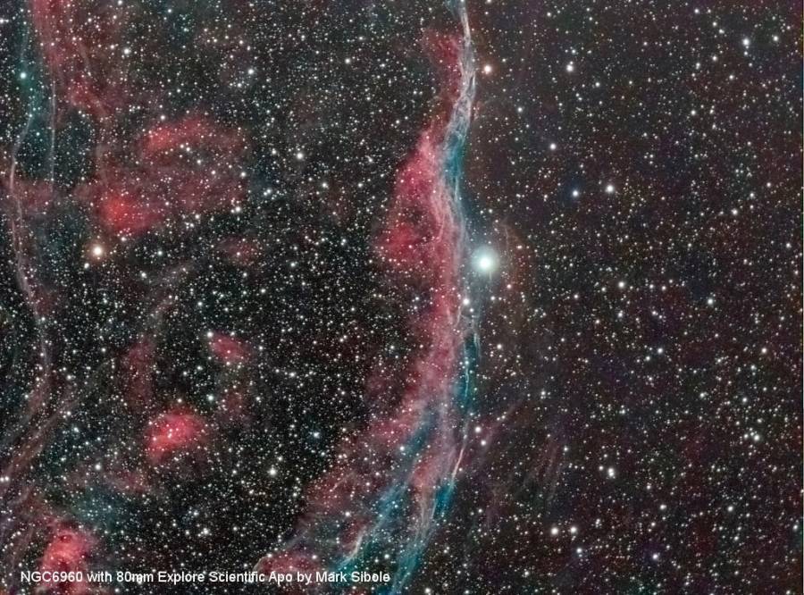 Het beeld toont de ruimtenevel NGC 6960, met rode en blauwe kleurwervels en een stralende ster in het midden.