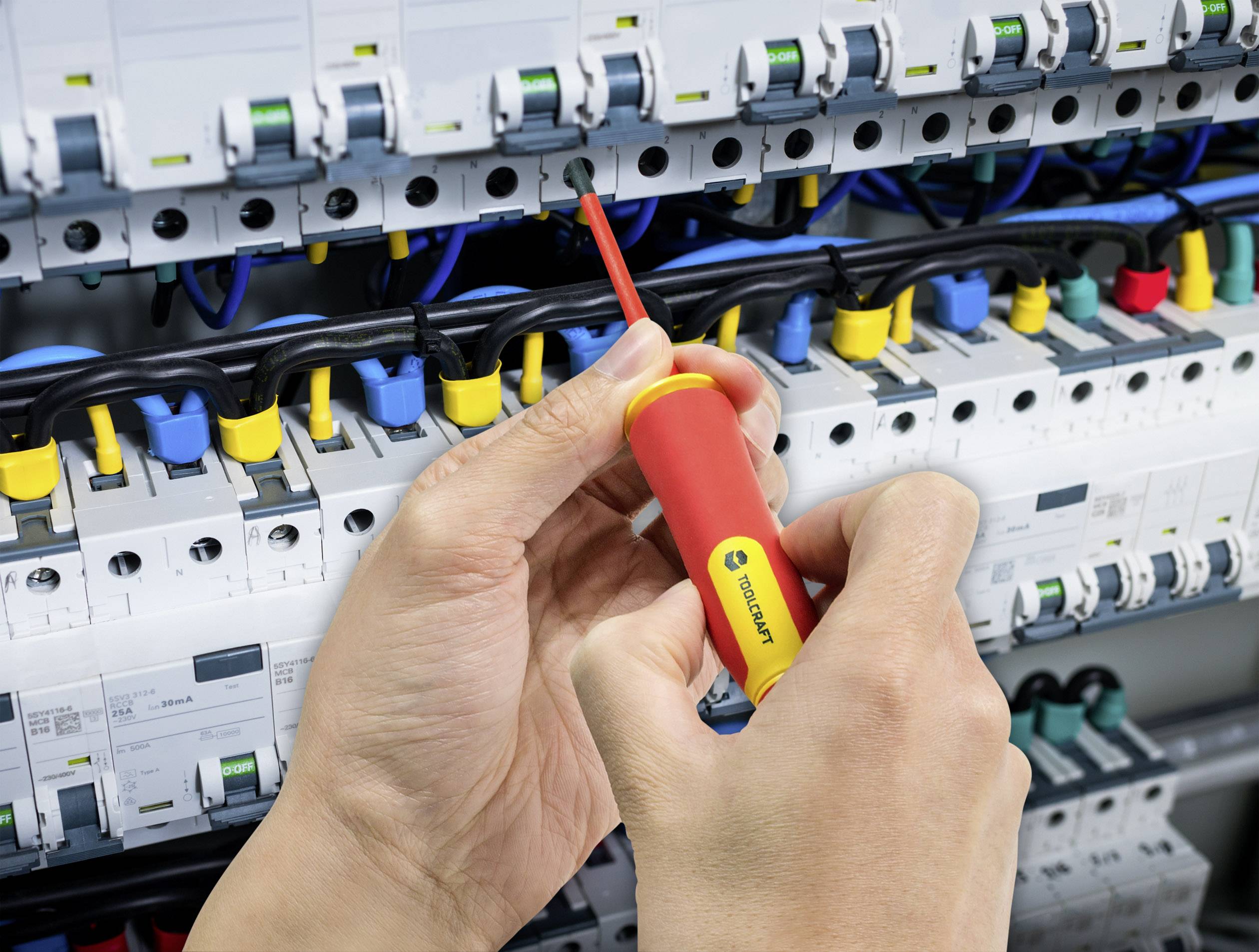 Een persoon gebruikt een schroevendraaier om kabels aan te sluiten op een elektrisch schakelbord. Verschillende gekleurde kabels zijn zichtbaar.