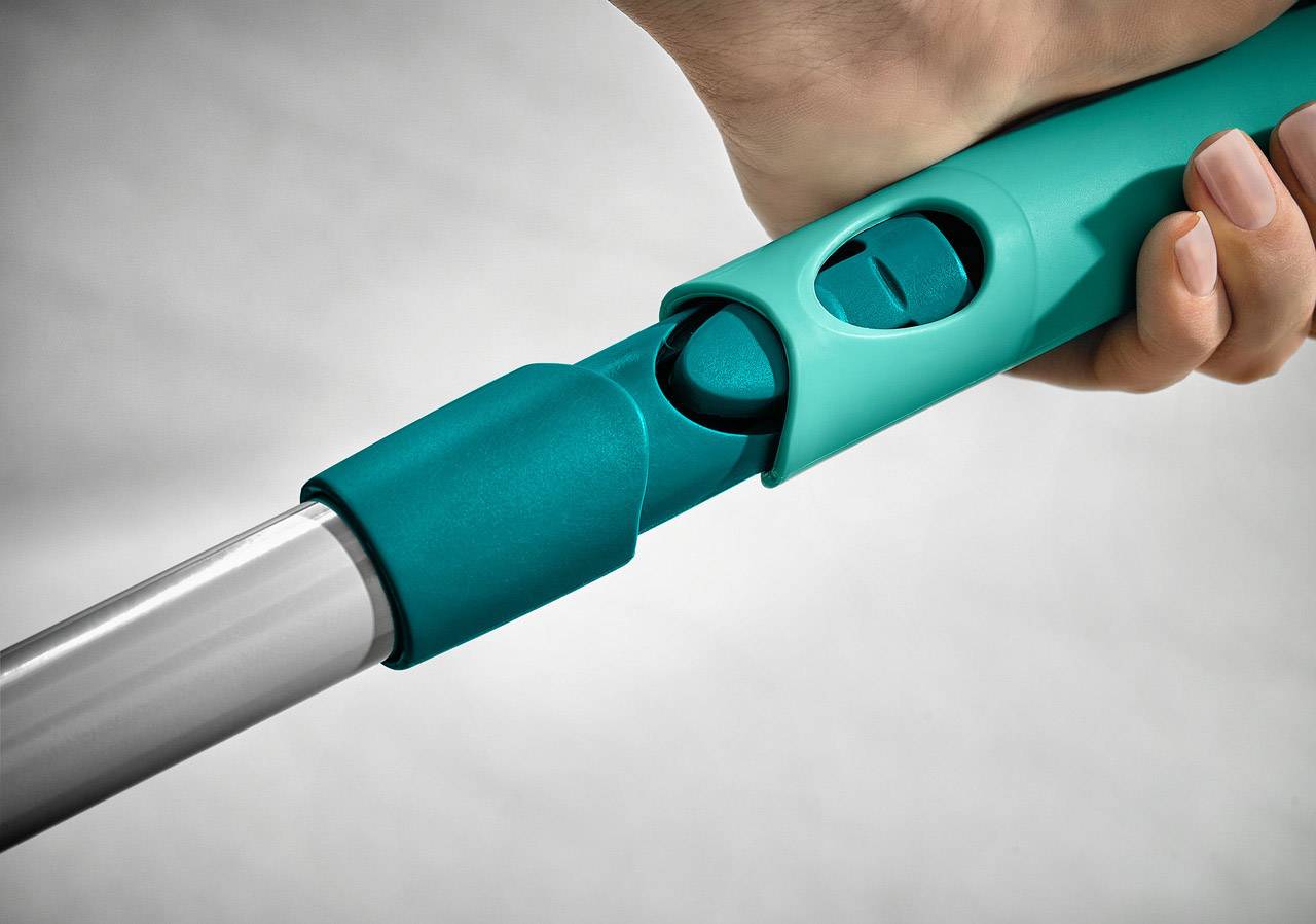 Een hand houdt een turquoise staaf vast met een vergrendelingsmechanisme. De staaf lijkt een stevig, verstelbaar handvat te zijn.