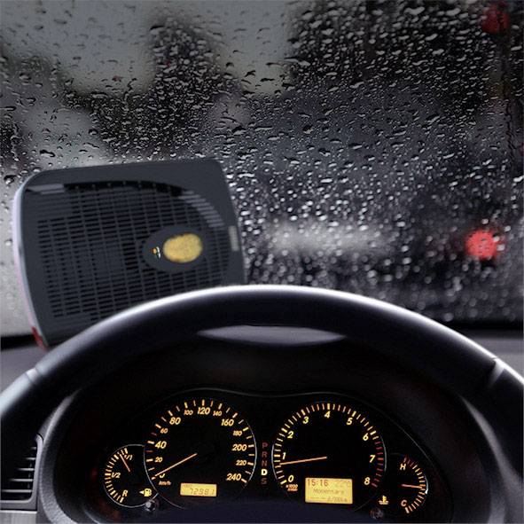 Een auto-interieur met een ontvochtigd, beslaginvrij raam. Een verwarmingsapparaat staat op het dashboard. Buiten valt regen.