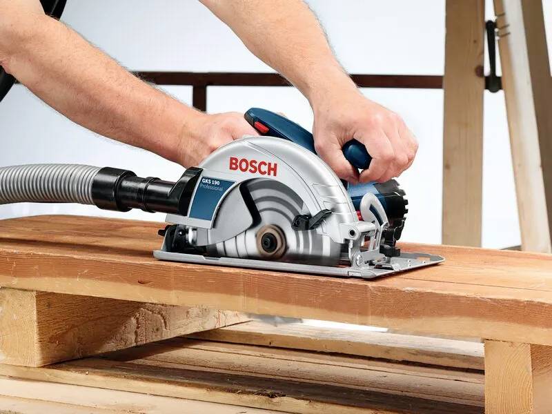 'Een persoon die een Bosch cirkelzaag gebruikt om een houten plank te zagen, waarbij hij een houtbewerkingstaak met precisie demonstreert.'