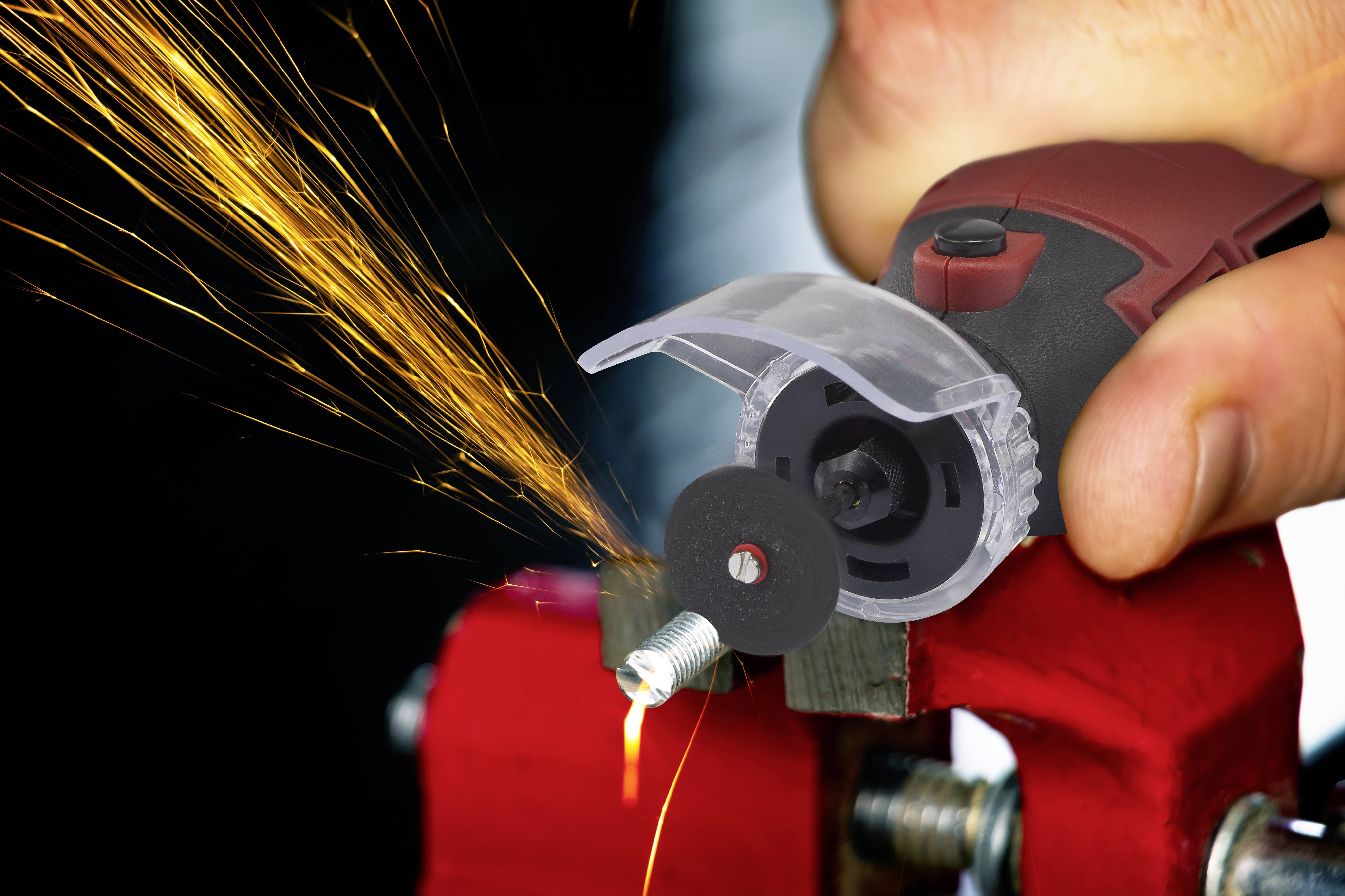 Een persoon slijpt een metalen schroefkop met een rode haakse slijper. Vonken spatten op vanaf het slijppunt.