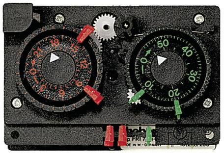 Een mechanische timer met twee wijzerplaten; links voor de tijd, rechts voor minuut-intervalinstellingen met gekleurde pinnen.