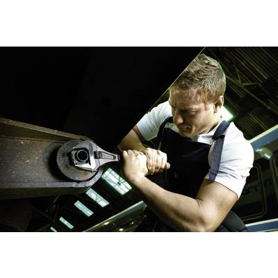 Een man in werkkleding gebruikt een grote moersleutel om aan een metalen onderdeel te werken, waarschijnlijk in een werkplaats.