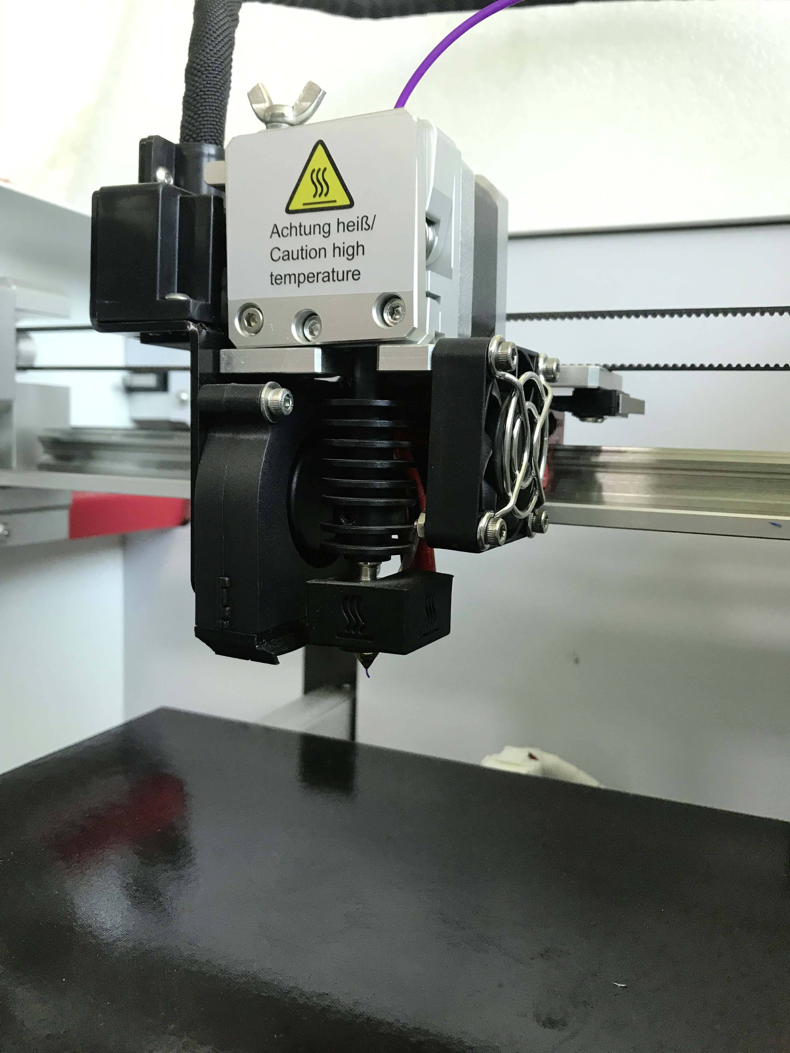3D-printer met waarschuwingsbord 'Let op, heet!/Caution high temperature'. Close-up van de printkop tijdens het afdrukken.