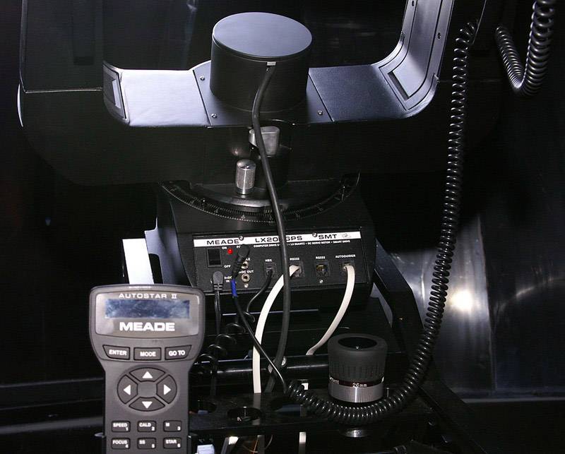 Een telescoop met elektronische besturingseenheid en bedieningspaneel. Kabels zijn aangesloten, en een hoofdapparaat toont 'Meade LX90'.