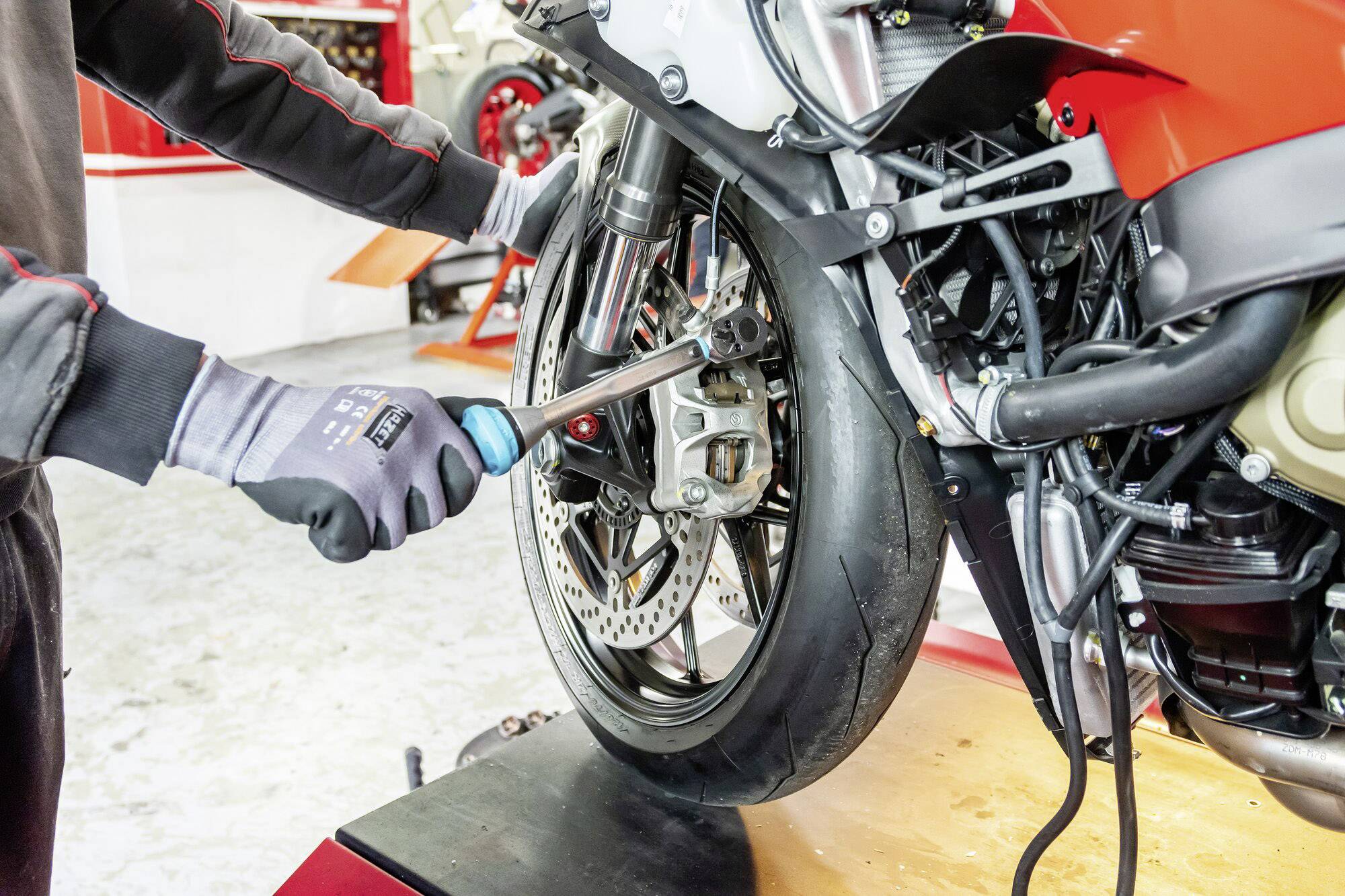 Een persoon repareert het voorwiel van een motorfiets op een werkbank terwijl hij ermee bezig is met behulp van een moersleutel.