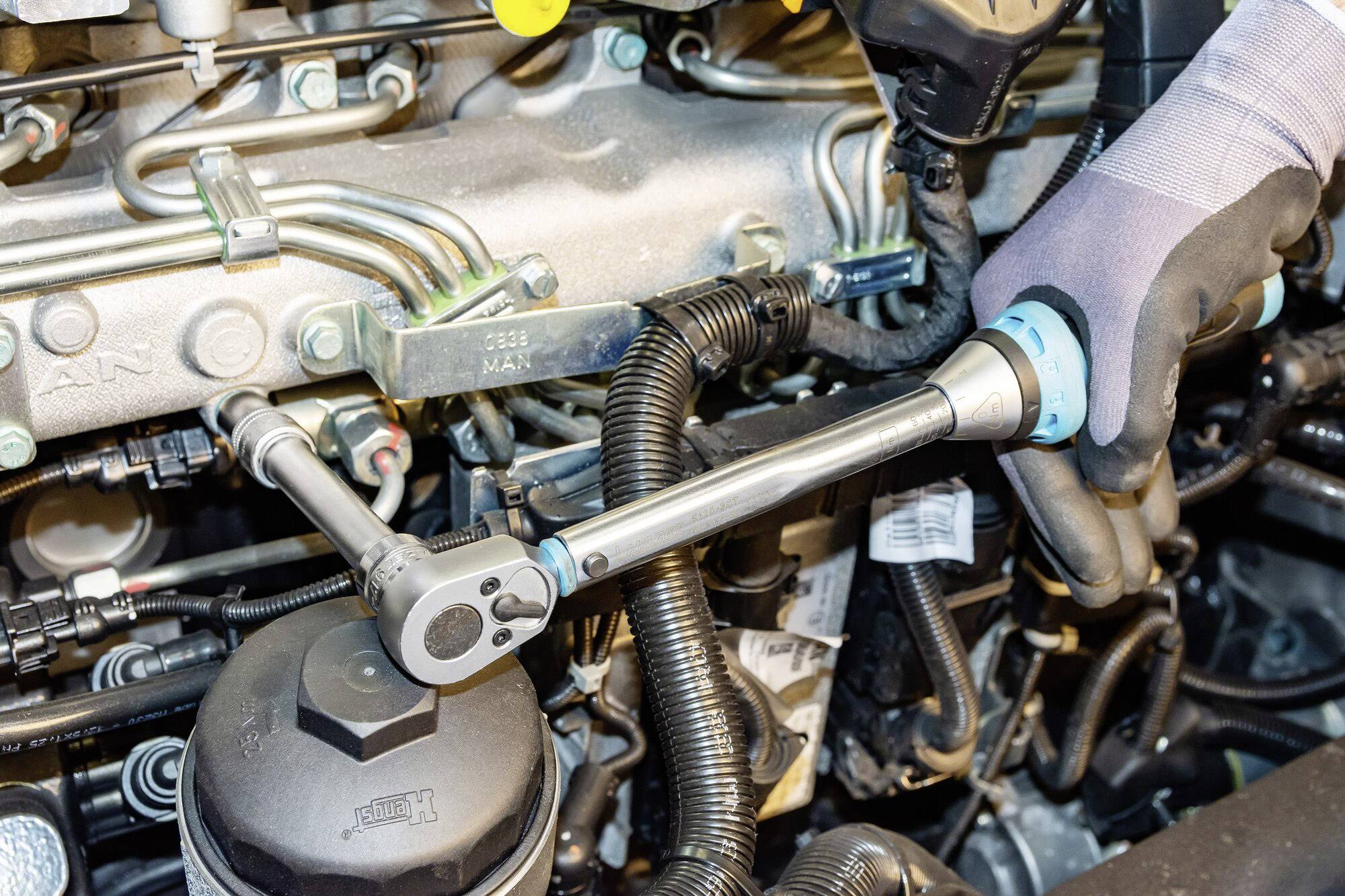 Een persoon trekt de bouten van een voertuigmotor aan met een momentsleutel. De motor is gedeeltelijk zichtbaar.