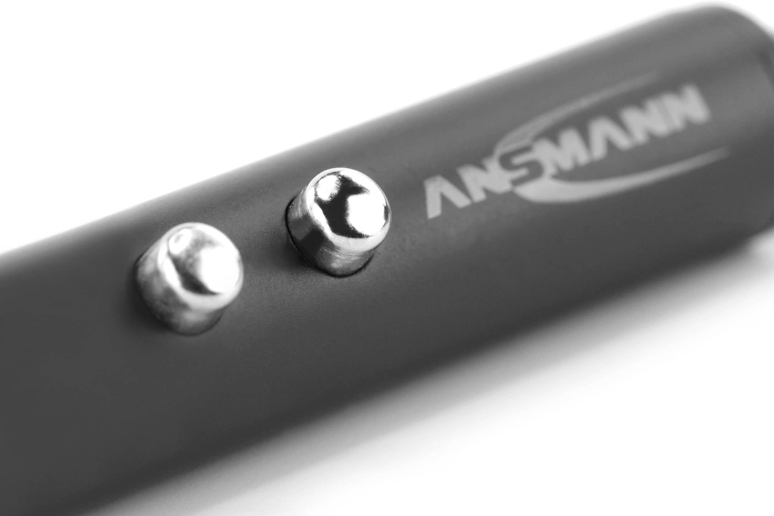 Close-up van een zwart apparaat met twee zilveren knoppen en het onscherpe logo 'ANSMANN' erop.