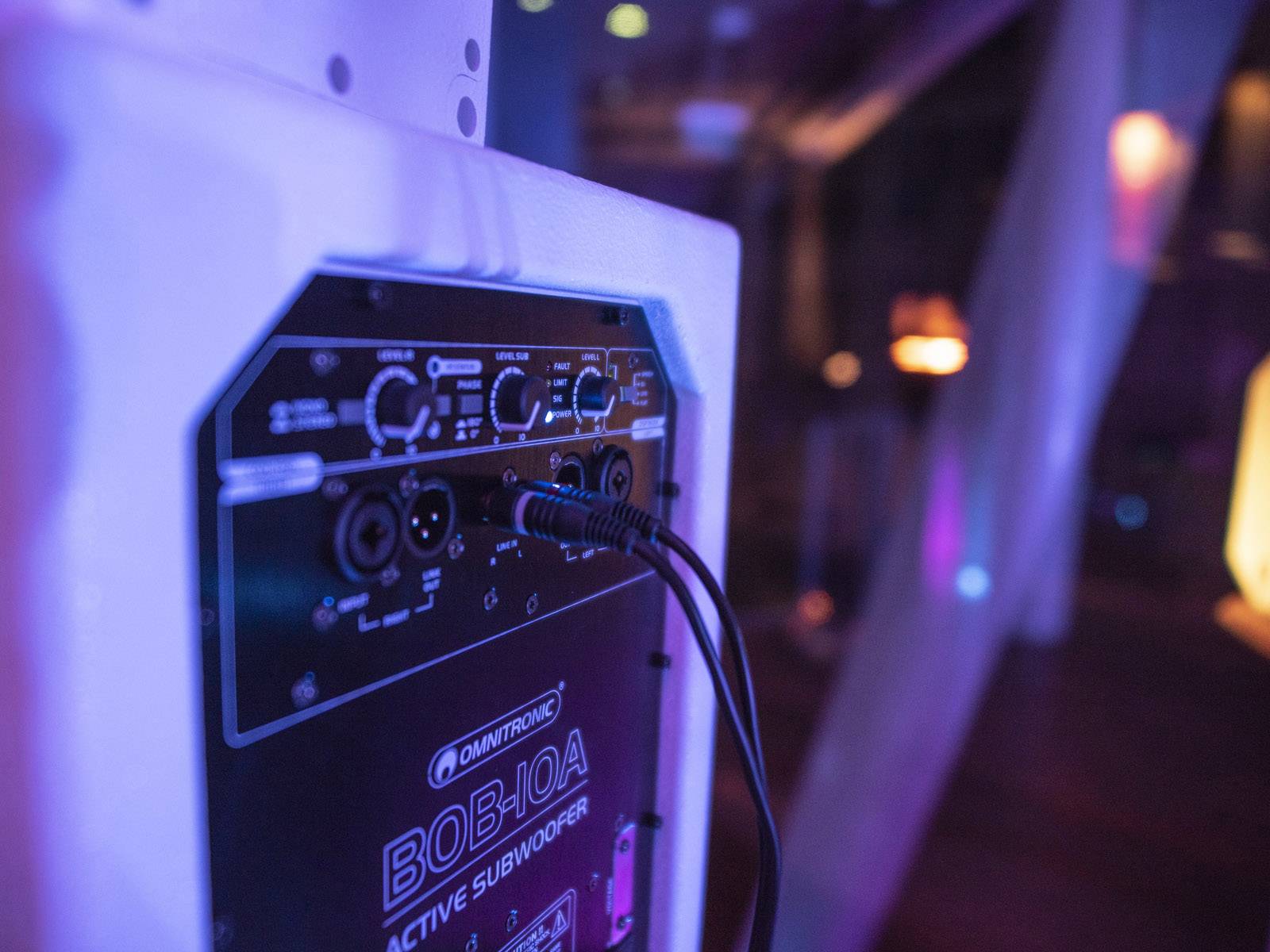 Achterkant van een actieve subwoofer met verschillende aansluitingsmogelijkheden in een sfeervol verlichte omgeving.