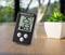 Digitale thermometer en hygrometer op een tafel tonen 25,1 graden Celsius en 63% luchtvochtigheid. Ernaast staat een kleine plant.