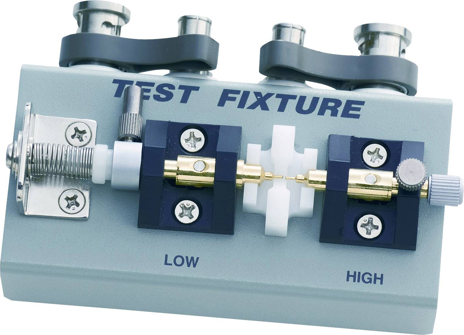 Testopstelling voor metingen met het opschrift 'Test Fixture'. Twee aansluitingen en een schroefmechanisme zijn zichtbaar.