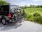 Zwarte bestelwagen met drie fietsen op een achterdrager, geparkeerd langs een landweg naast een groen veld met bomen op de achtergrond.