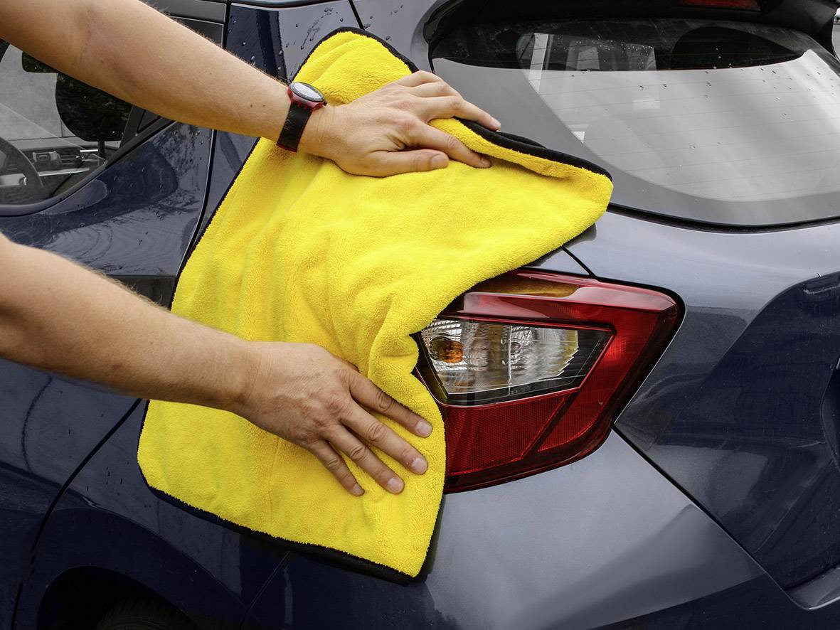 Een persoon reinigt het achterlicht van een auto met een geel doek. Handen zijn zichtbaar op het doek.