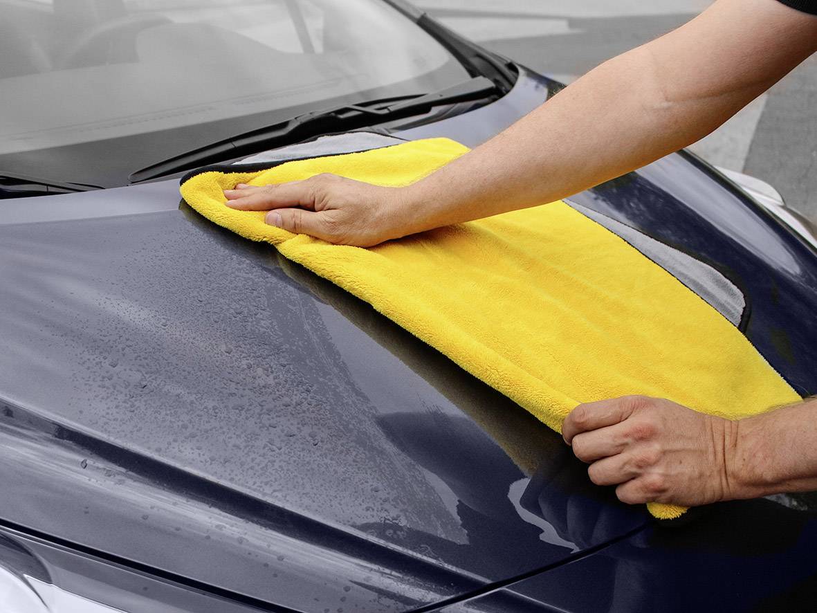 Een persoon veegt de motorkap van een auto schoon met een gele doek.