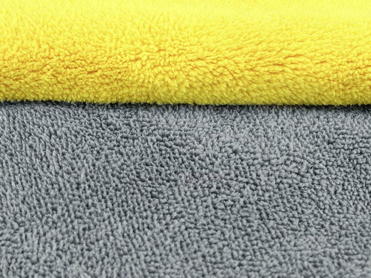 Een geel en een grijs badhanddoek van badstof liggen over elkaar heen.