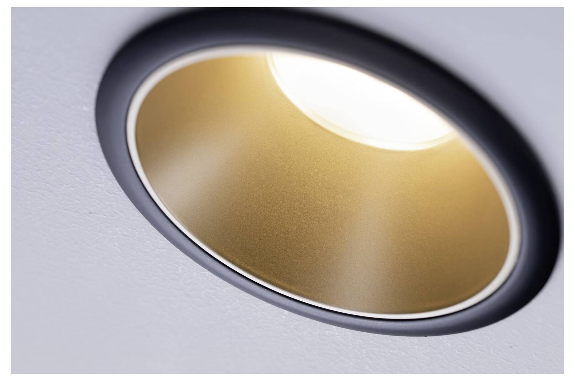 Plafondspot in close-up met een ronde, gouden binnenkant en zwarte rand, straalt warm licht in de ruimte.