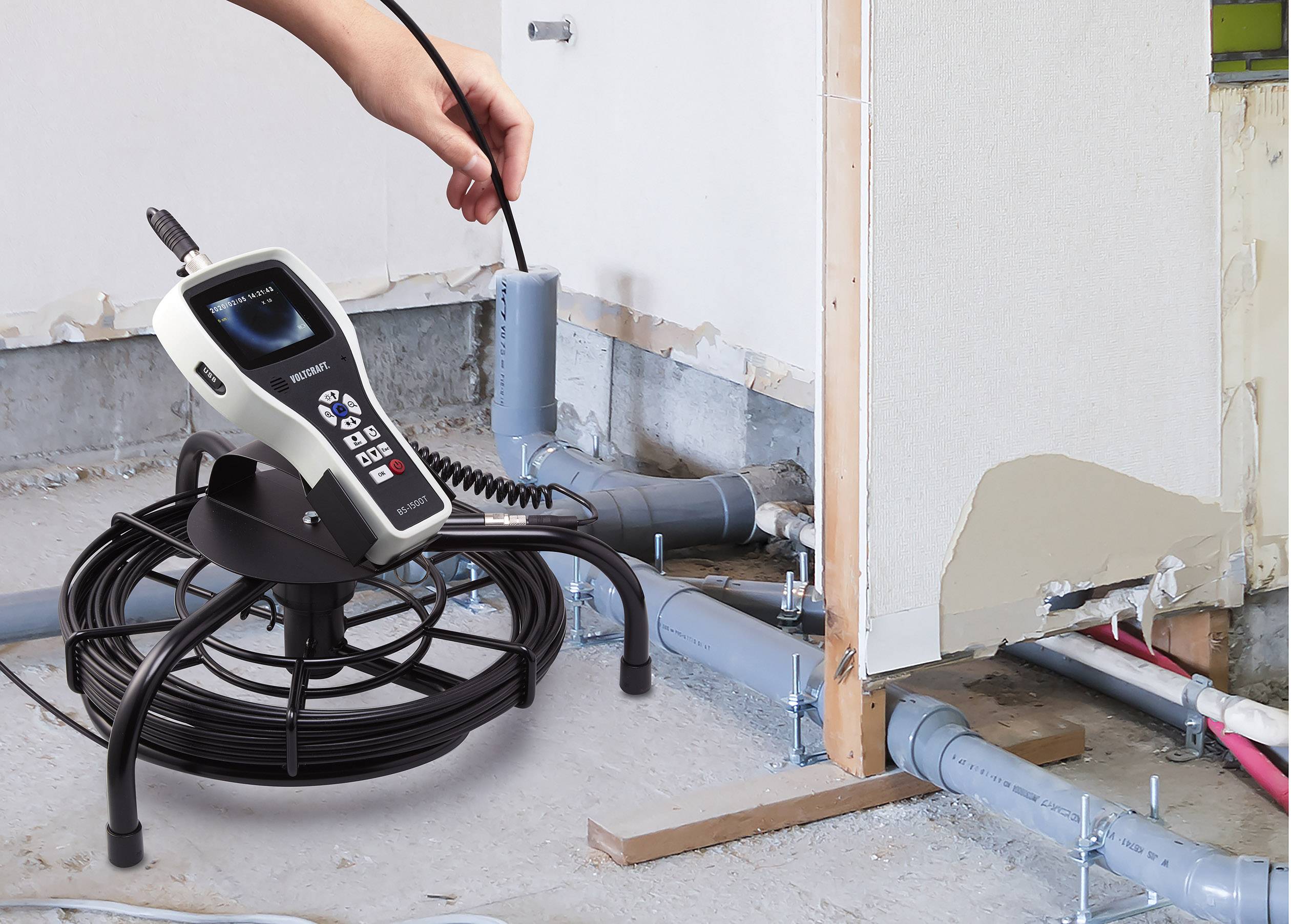 Een hand houdt een inspectie-endoscoop boven een afvoerbuis in een onafgewerkte muur. Het apparaat toont beelden van de binnenkant van de buis.