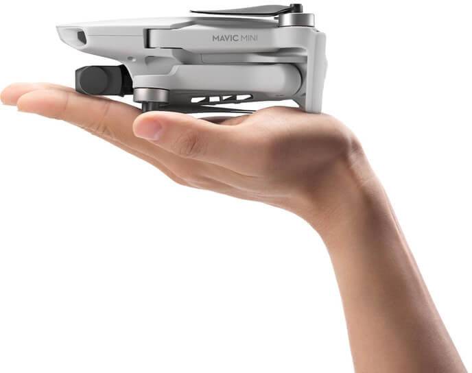 Een hand houdt een compacte, opgevouwen drone. De drone is klein en handzaam. De bovenkant toont het opschrift 'Mavic Mini'.