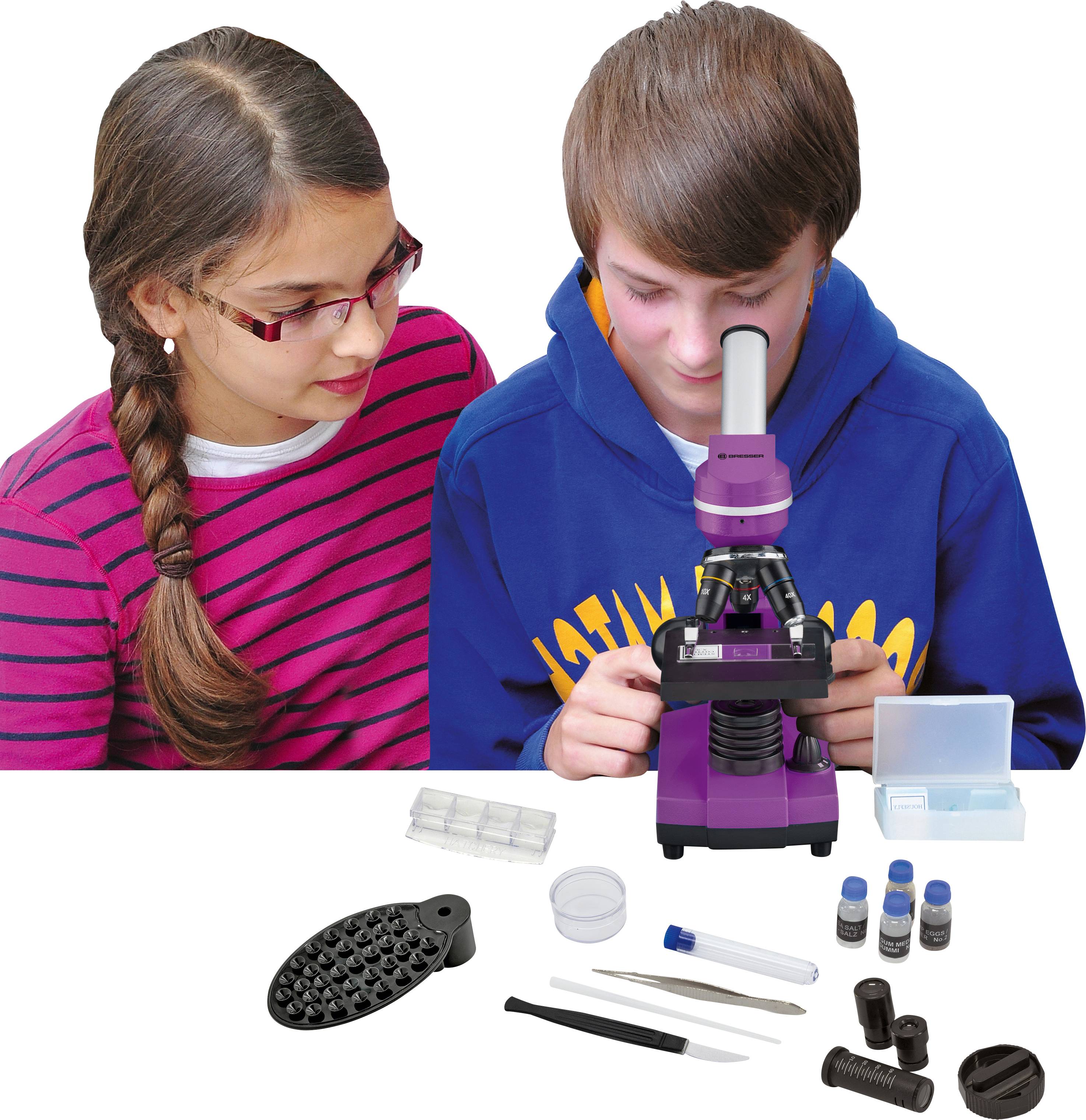 Twee kinderen bekijken een paarse microscoop. Op tafel liggen accessoires zoals objectglaasjes, pipet en containers.