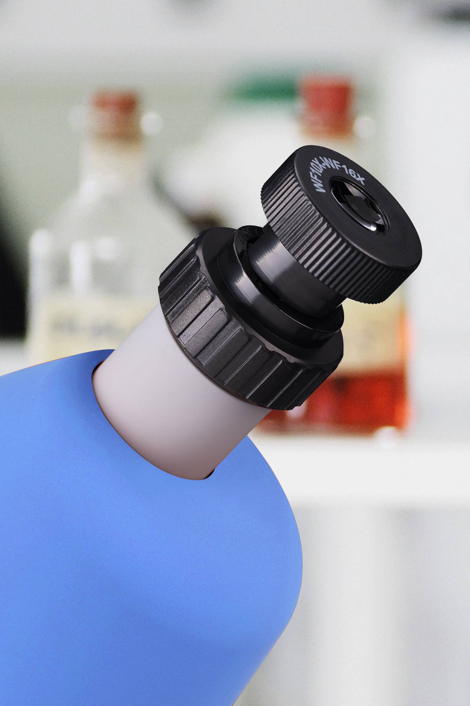 Close-up van een blauw microscoop, schuin gehouden, met focus op het oculair, onscherpe achtergrond toont flessen.